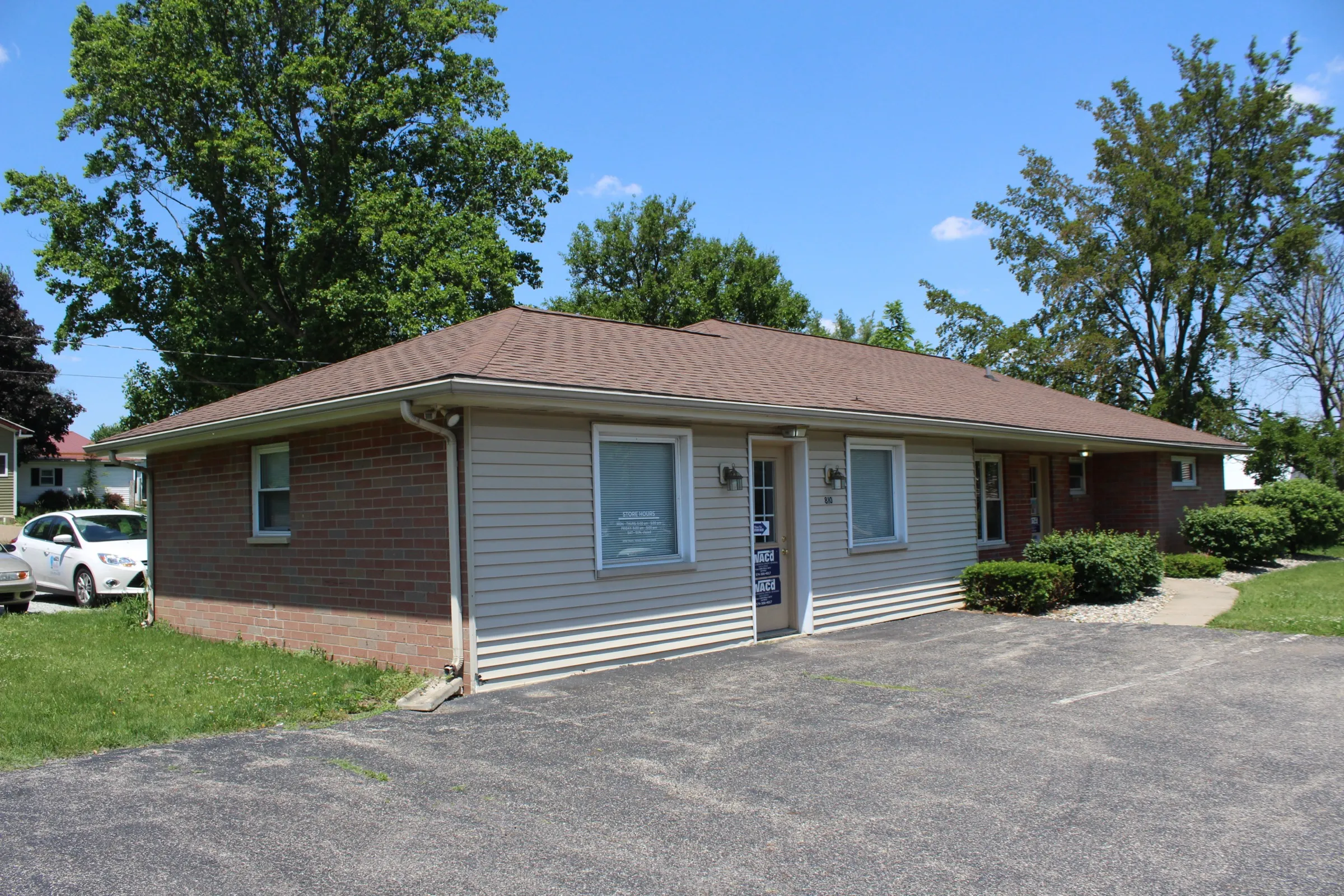 Side view of 810 South Buffalo Street with a paved parking area and trimmed shrubs along the brick and siding walls
