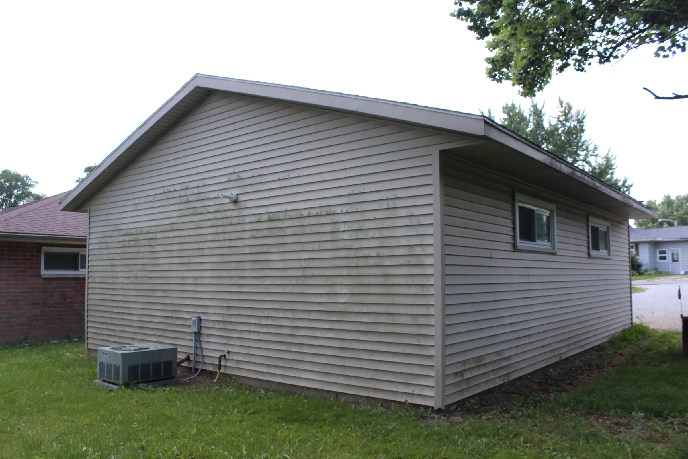 Back and side of the garage with two small windows and an outdoor air conditioning unit